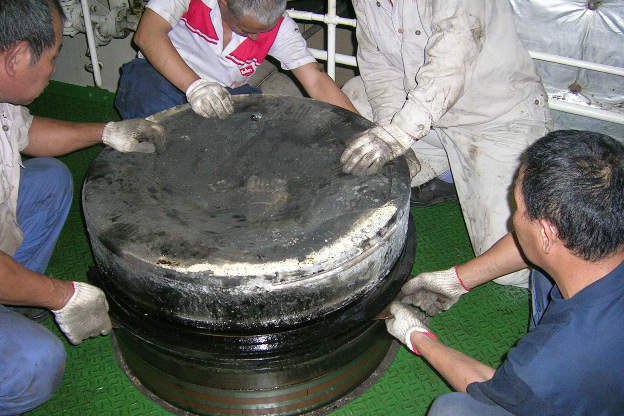Four crew members handling a piston on the engine room deck plates